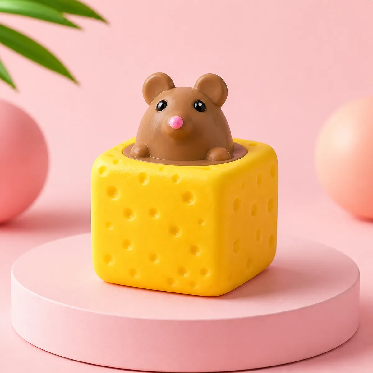 Żółty gniotek squishy w kształcie kostki sera z brązową myszką wyglądającą z góry na różowym podeście