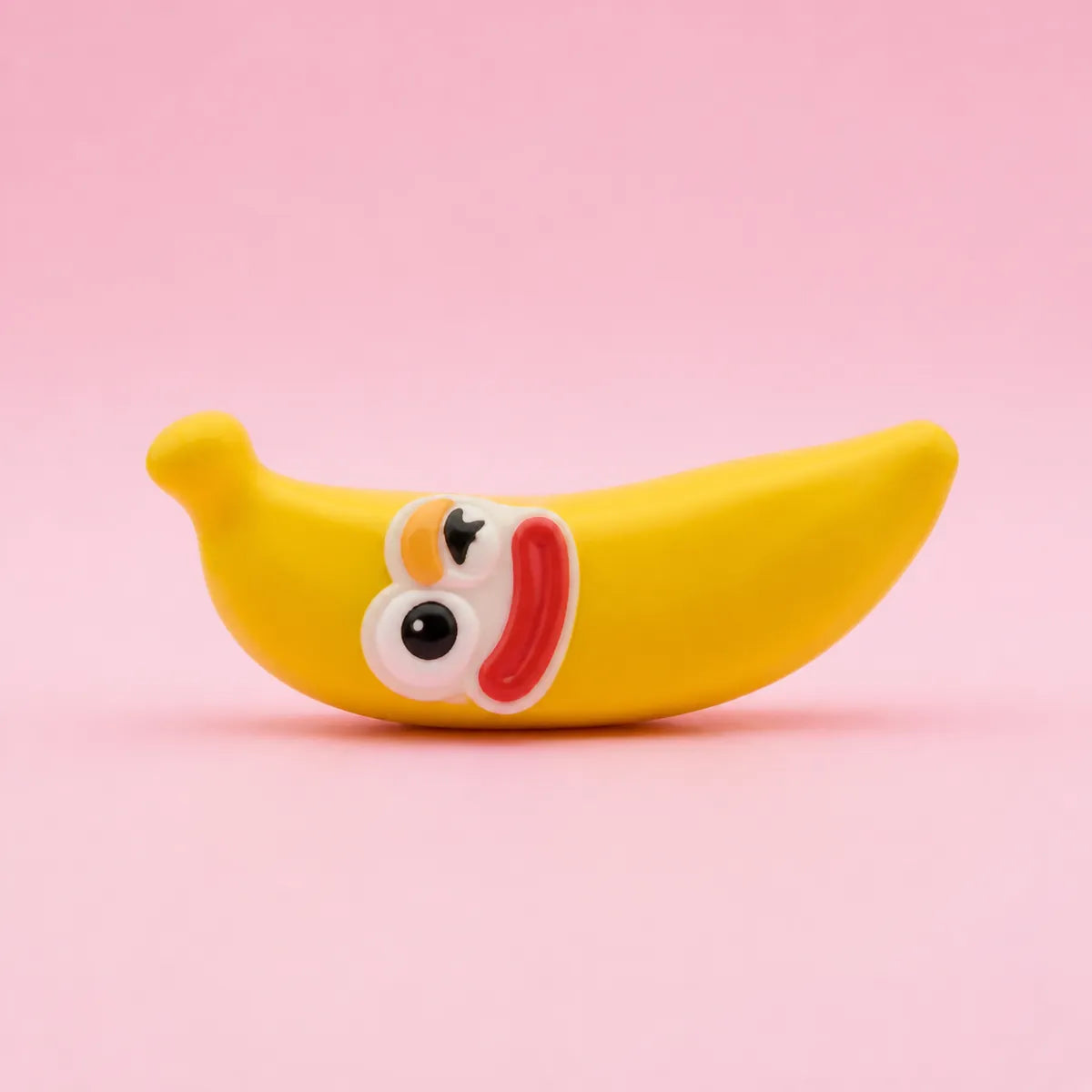 Żółty gniotek squishy w kształcie banana z uśmiechniętą buźką na różowym tle