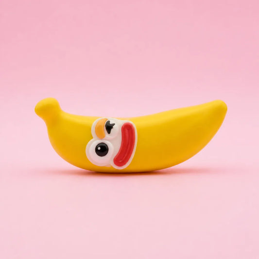 Żółty gniotek squishy w kształcie banana z uśmiechniętą buźką na różowym tle