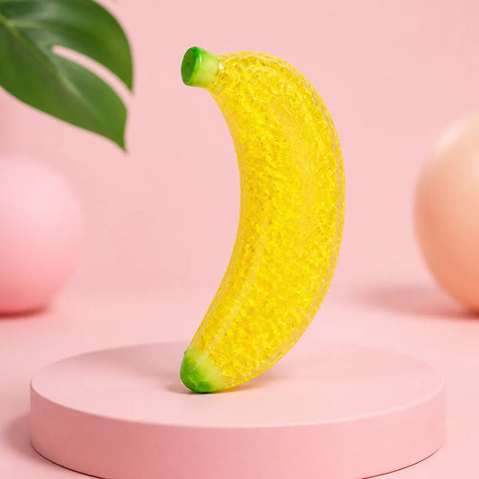 Żółty żelowy gniotek squishy w kształcie banana z zielonymi końcówkami na różowym podeście