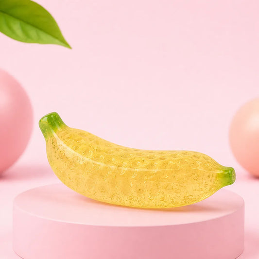 Żółty półprzezroczysty żelowy gniotek squishy w kształcie banana leżący na boku na okrągłym różowym podeście
