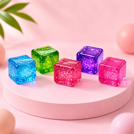 Pięć przezroczystych żelowych gniotków squishy w kształcie kostek: niebieska, zielona, czerwona, fioletowa i różowa na różowym podeście