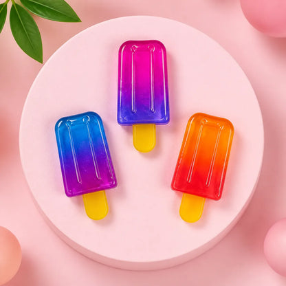 Trzy gniotki squishy w kształcie lodów na patyku: niebiesko-fioletowy, różowo-fioletowy i pomarańczowo-czerwony na okrągłym różowym podeście