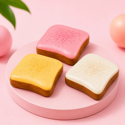 Trzy gniotki squishy w kształcie tostów: różowy, żółty i biały z brązowym spodem na okrągłym różowym podeście
